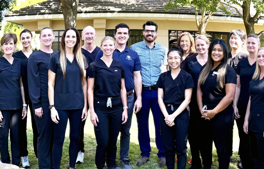The El Dorado Hills Dental team, sixteen people, most in black scrubs, with Dr. Austin Cope in a navy polo and Dr. Ben Cope in a blue patterned shirt, standing on a lawn in 2024.